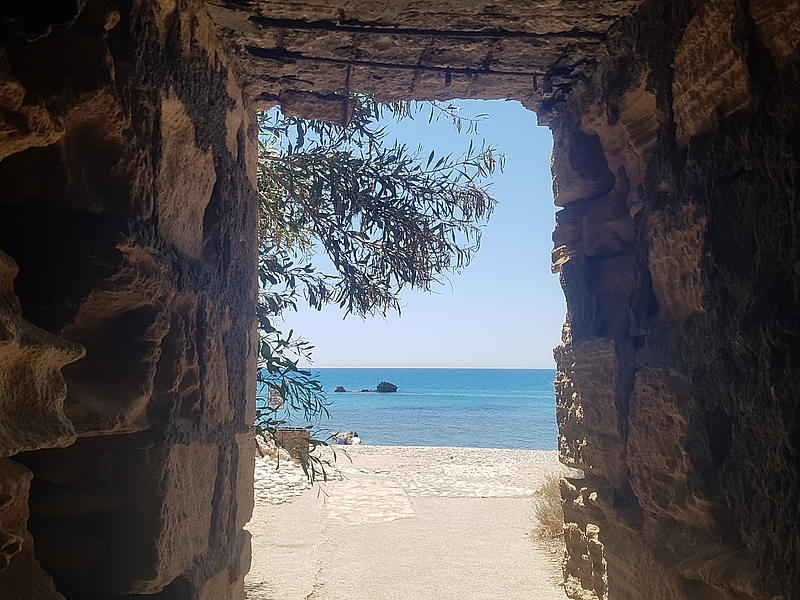 WeGoForPeaceTrip_Cyprus Stone gate with view of beach, sea and branch in the sunlight